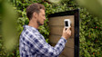 Article Header Image showing a neighbor installing the Outdoor Cam (2nd Gen) on the exterior of a modern home.