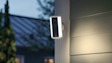 Ring Spotlight Camera (2nd Gen) mounted on the exterior siding of a modern home with the spotlights illuminated at dusk.