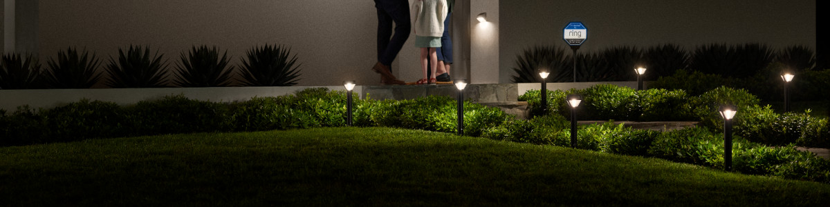 An assortment of Ring Smart Lighting products lighting up a homeowner's front yard at night.