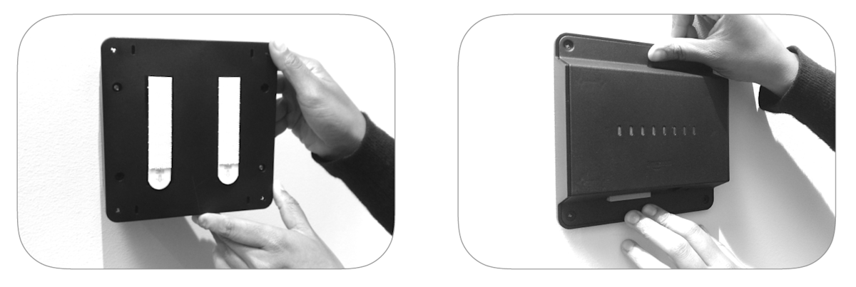 Hands installing black mounting bracket on wall with command strips.