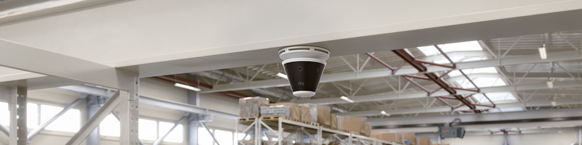 A photograph of a Ring Elite camera mounted on a ceiling in a warehouse.