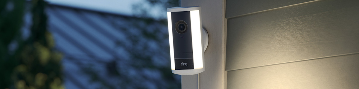Ring Spotlight Camera (2nd Gen) mounted on the exterior siding of a modern home with the spotlights illuminated at dusk.