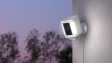 Ring Spotlight Cam Plus Plug-In mounted on a wall outside lighting up at sunset.