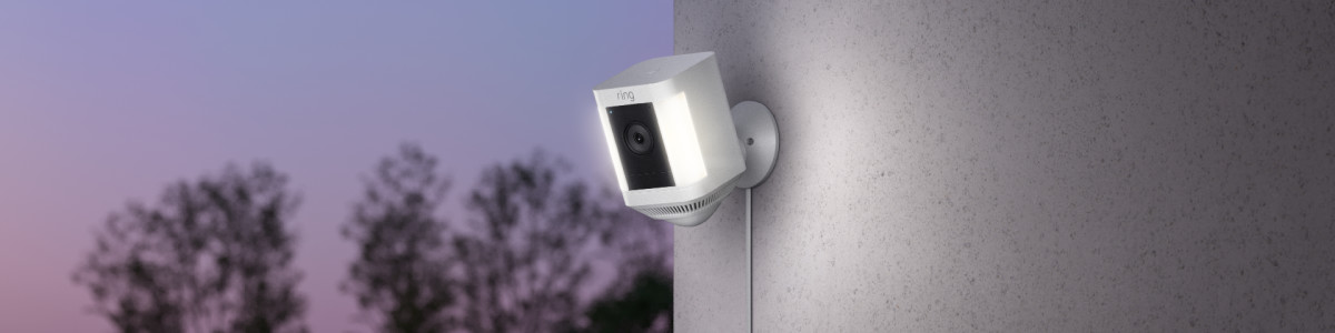 Ring Spotlight Cam Plus Plug-In mounted on a wall outside lighting up at sunset